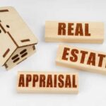 A small wooden model of a home and three small blocks spelling out the words Real Estate Appraisal