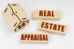A small wooden model of a home and three small blocks spelling out the words Real Estate Appraisal