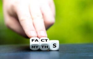A pair of dice are held up by a hand, revealing that they say "fact" on one side and "myth" on the other