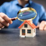 A man holds a magnifying glass over a model of a home