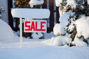 A for sale sign, covered in snow, in front of a house