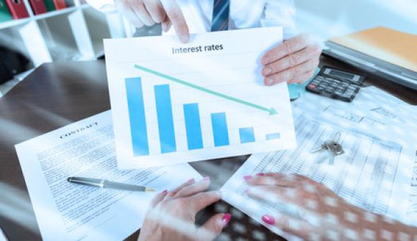 A person holds up a piece of paper that shows interest rates going down on a graph