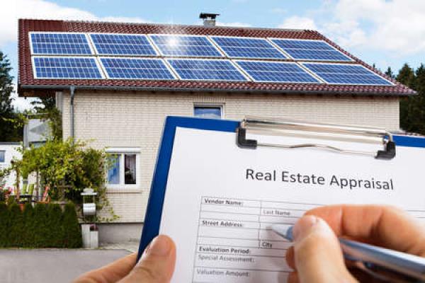 A clipboard that says "real estate appraisal" is held in front of a home