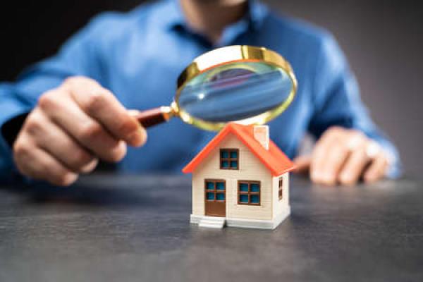 A man holds a magnifying glass over a model of a home