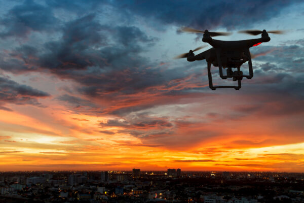 Silhouette of drone flying above city at sunset