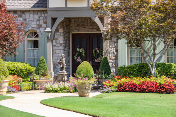 Entrance to upscale rock house with beautiful landscaping and a statue and wreaths and benches beside front porch