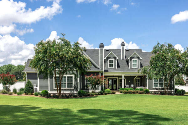 The rear view of a large gray craftsman new construction house with a landscaped yard and a garage and driveway.